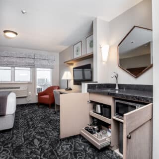 A hotel room with a sitting area, flat-screen TV, mini-fridge, microwave, coffee maker, and large window with city view.
