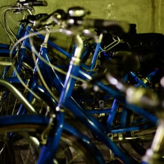 Several blue bicycles are parked close together in a dimly lit indoor bike rack.