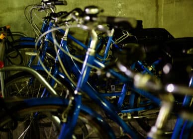 Several blue bicycles are parked close together in a dimly lit indoor bike rack.