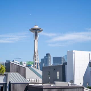 The Space Needle rises above modern buildings in downtown Seattle under a clear blue sky.
