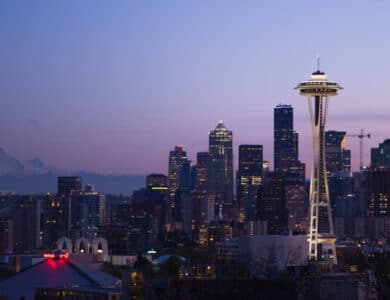 Seattle city skyline at dusk with the Space Needle in the foreground and Mount Rainier visible in the distance under a clear sky.