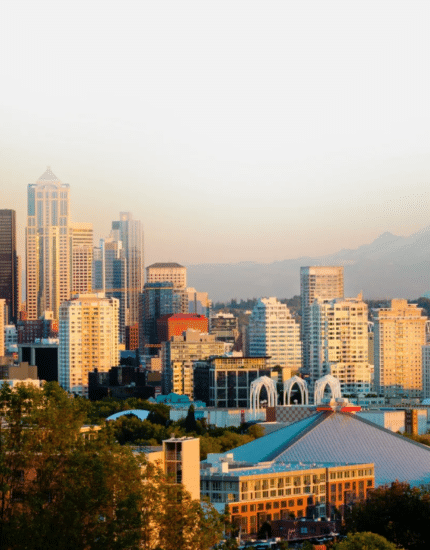 Seattle skyline at sunset with the Space Needle and Mount Rainier visible in the background under a clear sky.