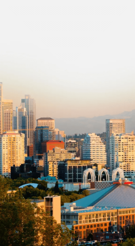 Seattle skyline at sunset with the Space Needle and Mount Rainier visible in the background under a clear sky.