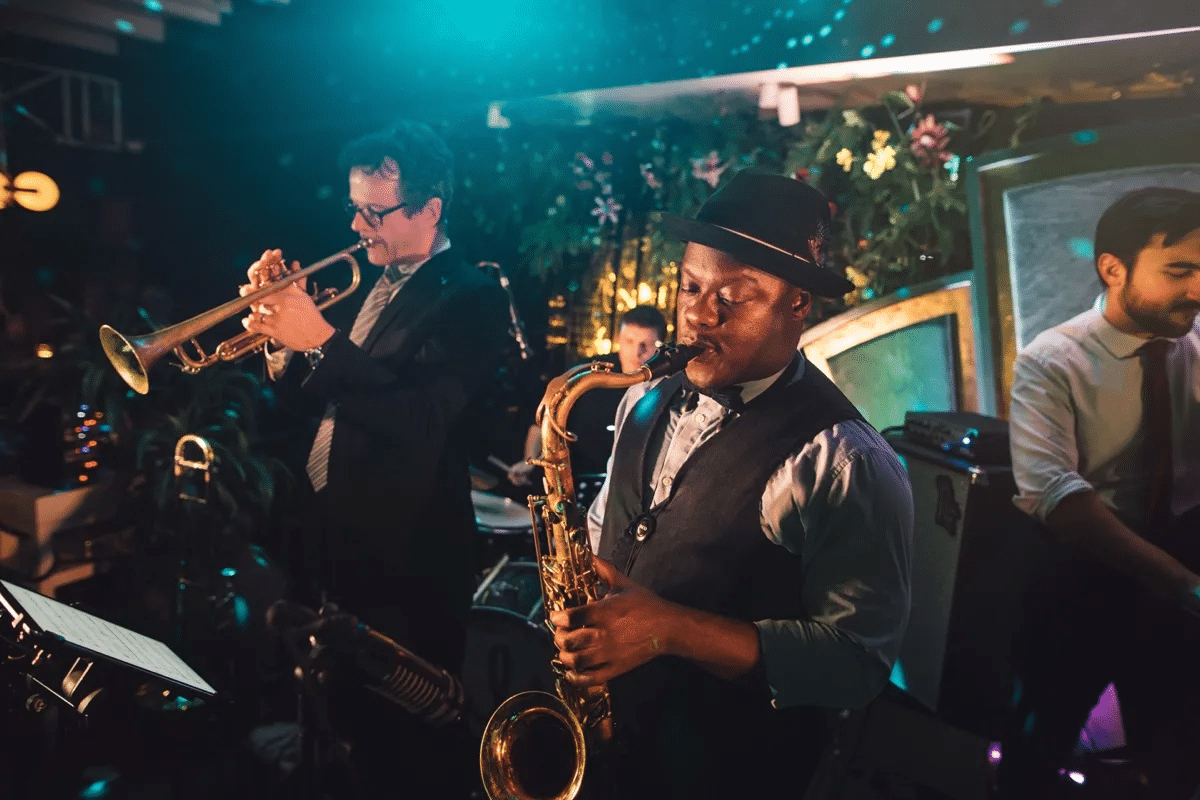 A jazz band performs on stage, featuring musicians playing trumpet, saxophone, and keyboard under warm, ambient lighting.