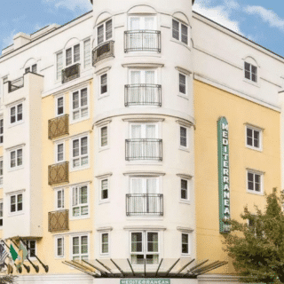 A multi-story Mediterranean-style hotel building with yellow and white exterior walls, numerous balconies, and a sign reading “MEDTERRANEAN” on the front.