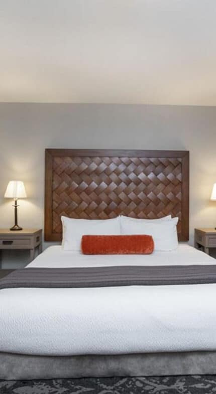 A hotel room with a large bed, two bedside tables with lamps, framed artwork on the wall, and a red upholstered chair in the corner.