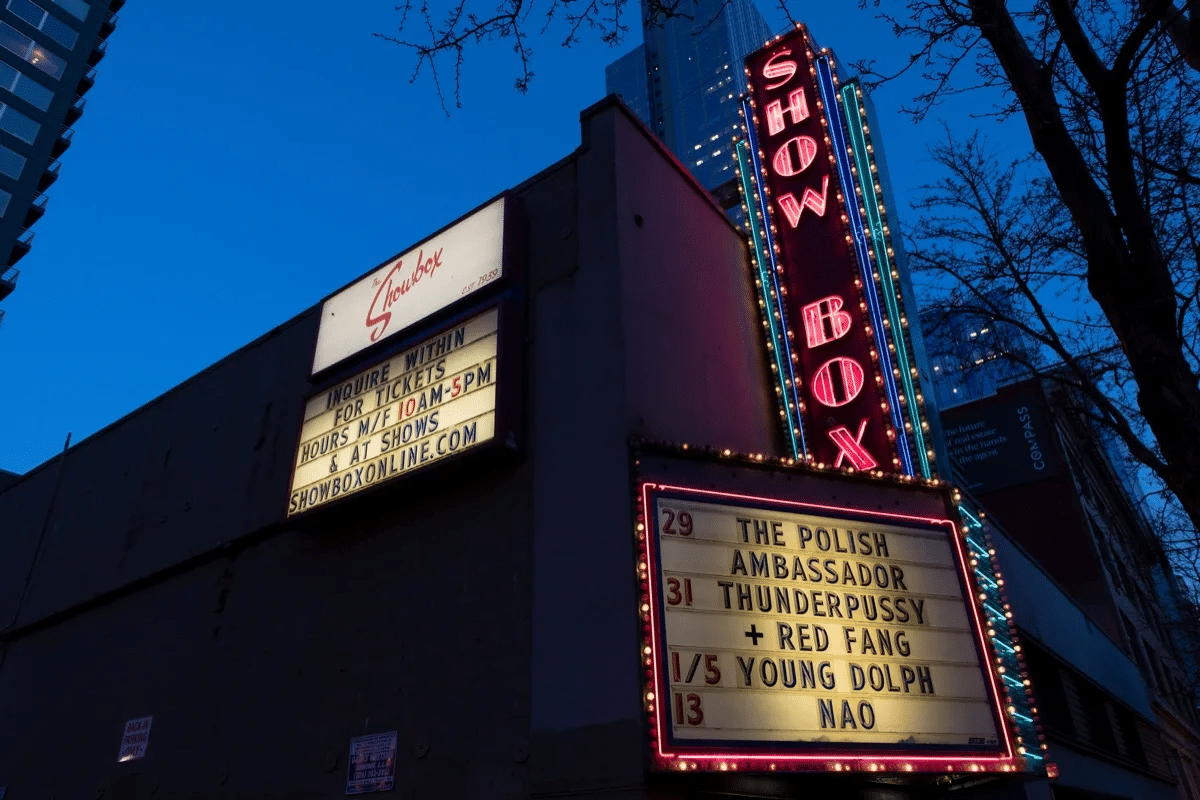 A theater at dusk with illuminated "Showbox" sign and marquee listing upcoming performances by The Polish Ambassador, Thunderpussy, Red Fang, Young Dolph, and Nao.