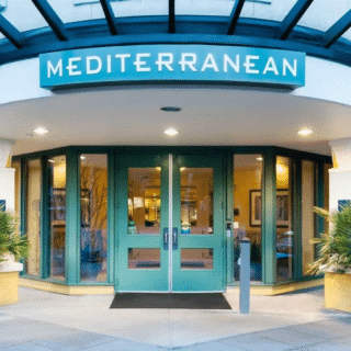 Entrance to a building with glass double doors and a green sign above labeled "Mediterranean"; potted plants are on either side of the doorway.